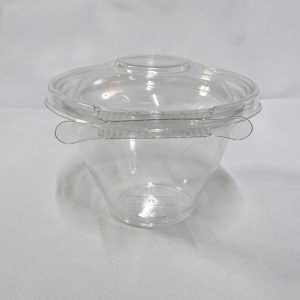 Envase redondo descartable de plástico transparente (PET) tipo estuche con base profunda y tapa chata. Se presenta en dos imágenes: una con el envase completamente abierto mostrando la profundidad de su cavidad inferior y la tapa unida por bisagra en segundo plano, y otra del envase cerrado visto de frente donde resalta la pestaña del precinto de seguridad perimetral, ambas sobre un fondo claro.