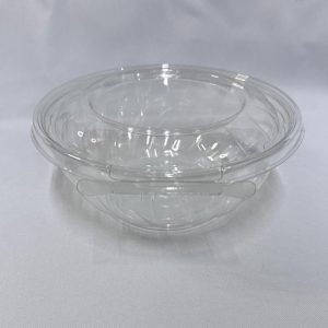 Dos ensaladeras redondas apiladas de plástico transparente (PET), mostrando la base profunda y la tapa con su diseño de cierre perimetral, vistas en ángulo desde arriba sobre un fondo claro.