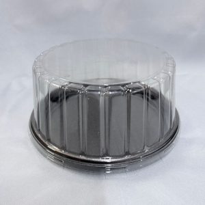 Envase redondo descartable para tortas con base de EPS color negro y tapa alta de plástico transparente con bordes acanalados, visto en ángulo desde arriba sobre un fondo blanco.