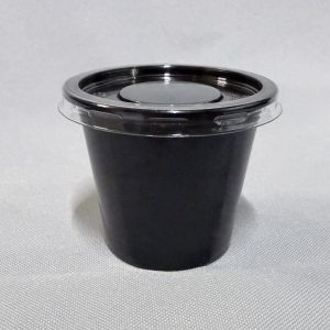 Pequeño pote salsero de plástico color negro con su tapa ajustada colocada, visto en ángulo desde arriba sobre un fondo claro.