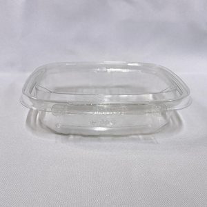 Envase cuadrado descartable de plástico transparente (PET) tipo estuche. Se muestra en dos vistas: una completamente abierto dejando ver su tapa unida por bisagra, y otra cerrado destacando la pestaña del precinto de seguridad frontal, ambas sobre un fondo claro.