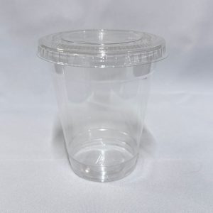 Vaso descartable de plástico PET ultra transparente equipado con una tapa plana que incluye una ranura central en forma de cruz para sorbete, visto en ángulo desde arriba sobre un fondo blanco.