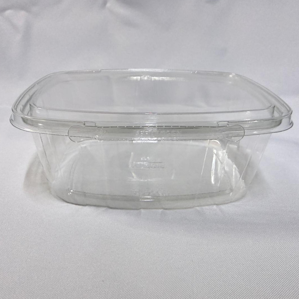 Envase rectangular descartable de plástico transparente (PET) tipo estuche de capacidad extra grande. Se presenta en dos imágenes: una mostrando el envase completamente abierto, dejando ver su interior súper profundo y amplio con la tapa unida por bisagra en segundo plano, y otra del envase cerrado visto de frente donde resalta la pestaña del precinto de seguridad con la inscripción "ABRA / OPEN", ambas sobre un fondo claro.