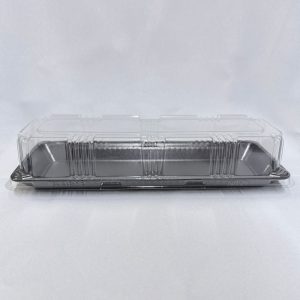 Envase rectangular muy alargado descartable, compuesto por una base chata de espuma color negro y una tapa alta de plástico transparente con detalles acanalados, visto de frente sobre un fondo claro.