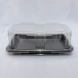 Envase rectangular descartable compuesto por una base chata de espuma color negro y una tapa alta de plástico transparente con detalles acanalados, visto en ángulo frontal desde arriba sobre un fondo claro.