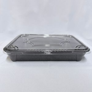 Envase rectangular descartable ancho para sushi, compuesto por una base profunda de espuma color negro y una tapa plana de plástico transparente con un diseño geométrico labrado en relieve, visto de frente sobre un fondo claro.