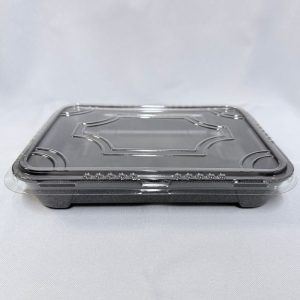 Envase rectangular descartable mediano para sushi, compuesto por una base de espuma color negro y una tapa plana de plástico transparente con un diseño geométrico labrado en relieve, visto de frente sobre un fondo claro.