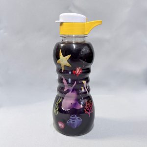 Botella plástica infantil de 350 ml con diseño ergonómico de centro acanalado y tapa amarilla con pico blanco. Se muestran diferentes vistas y dos diseños de estampados: uno de fondo oscuro con motivos marinos (un tiburón, una estrella de mar y peces) y otro de fondo claro con motivos de la selva (un cocodrilo, un tucán y un oso con la frase "Bichos da Floresta"), todas sobre un fondo claro.