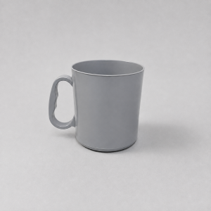 Taza escolar de plástico rígido en color gris claro, con asa ergonómica, fotografiada en un ligero ángulo sobre un fondo neutro gris.