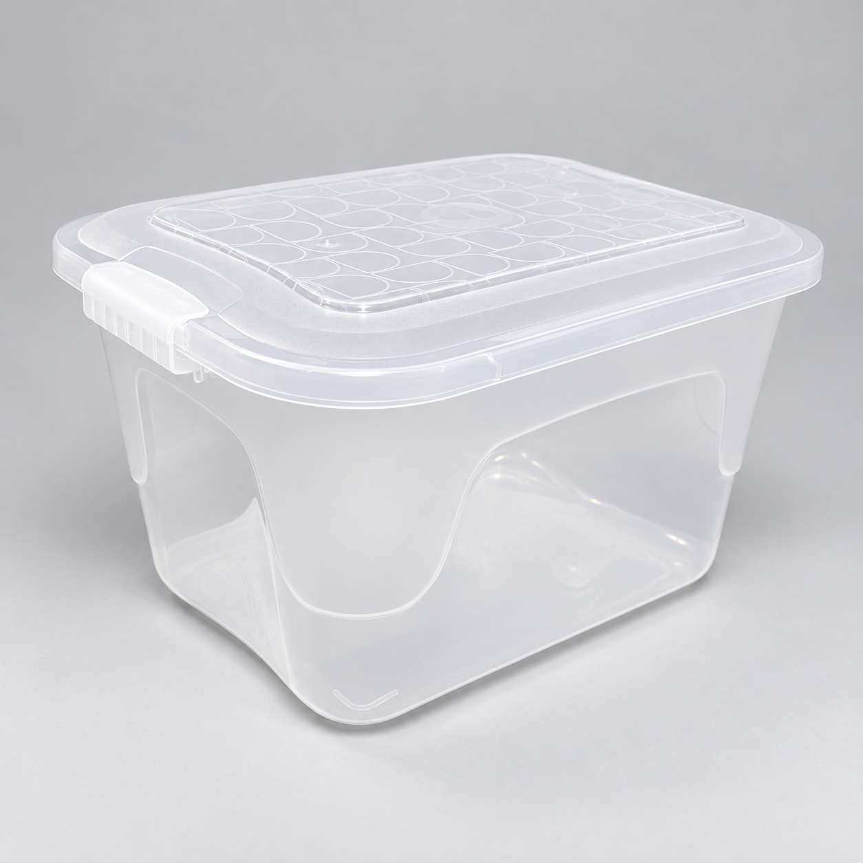 Vista superior en ángulo de una caja organizadora de plástico transparente. En la tapa se observa un patrón de líneas que forman semicírculos, un detalle central circular y trabas laterales en las asas para asegurar el cierre.