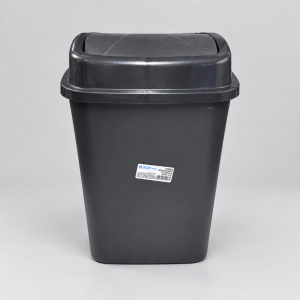 Vista frontal de una papelera rectangular de plástico color negro con tapa basculante cerrada, fotografiada sobre un fondo gris claro. En la parte inferior del frente lleva adherida una pequeña etiqueta blanca de la marca BUD Plastic.